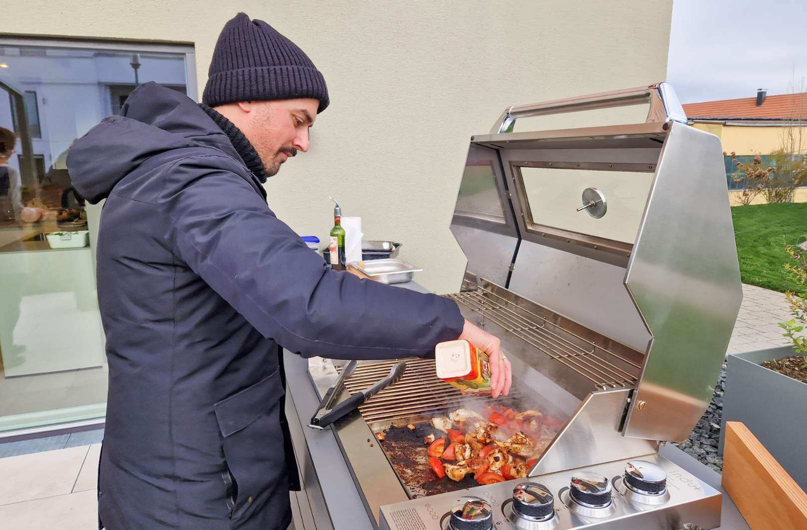 Mann grillt an Outdoorküche mit Grill bei kalten Temperaturen (Winterfest)